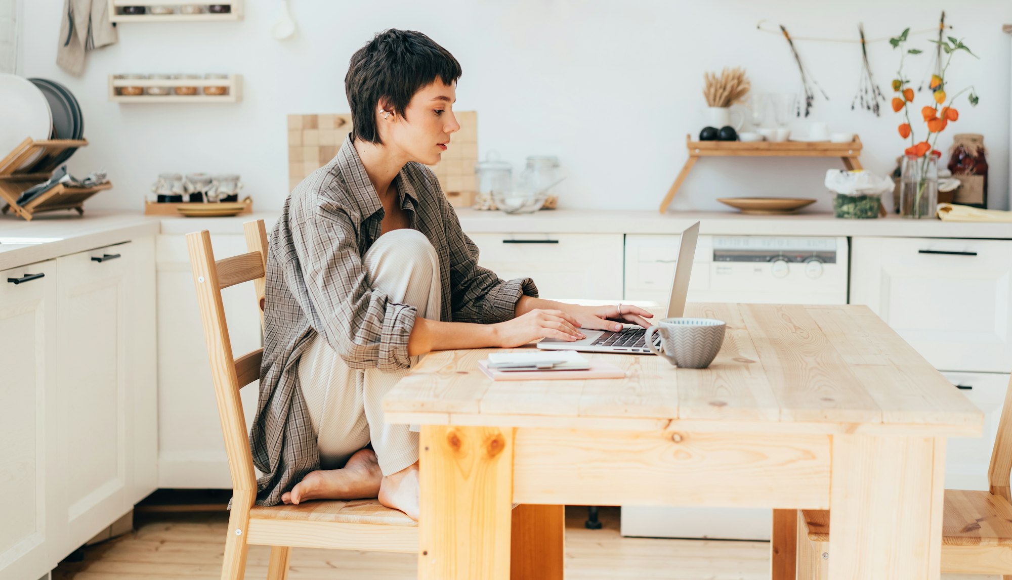 Woman freelancer sitting in the kitchen at home working on a laptop.